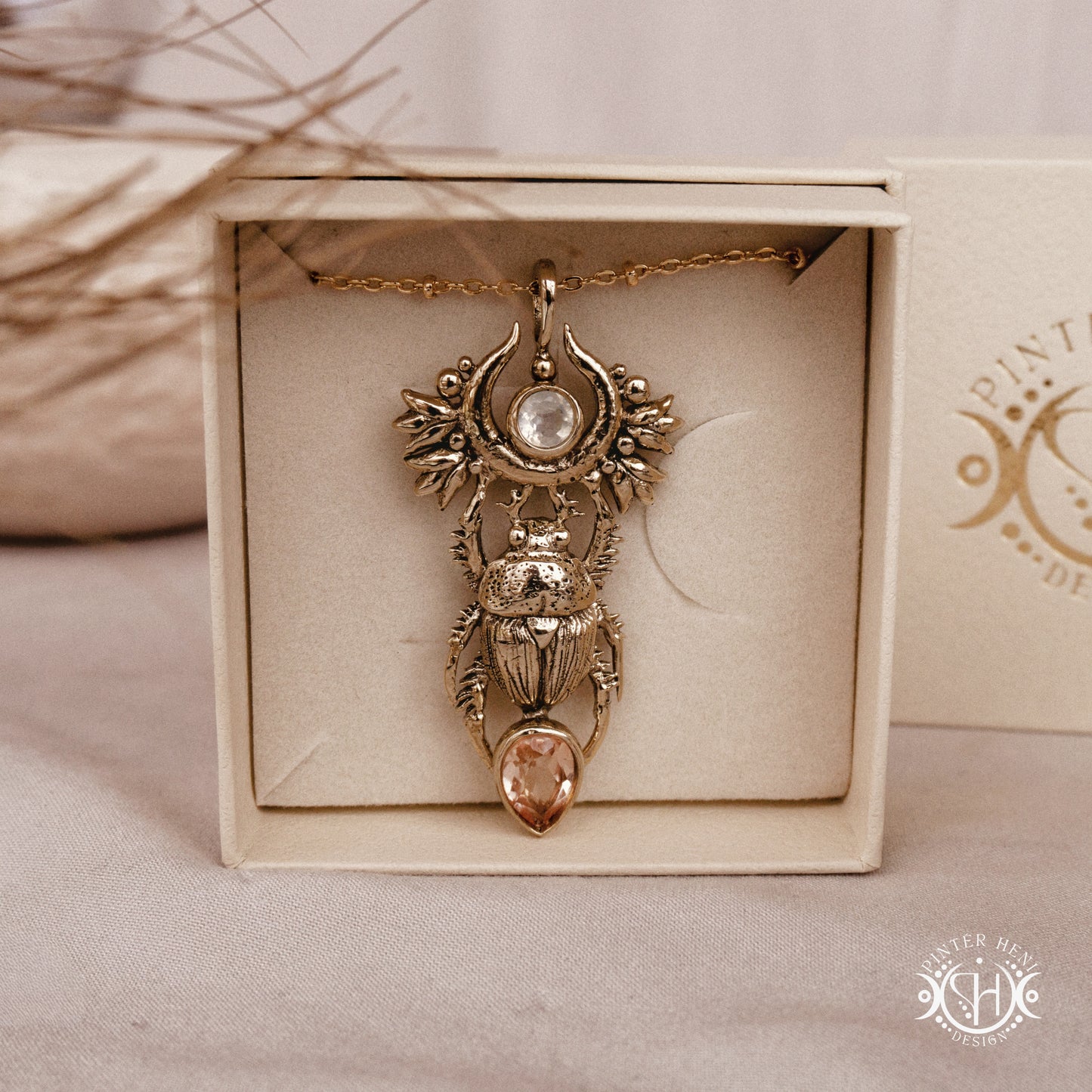 Brass scarab pendant with gemstones in a decorative box on a beige surface