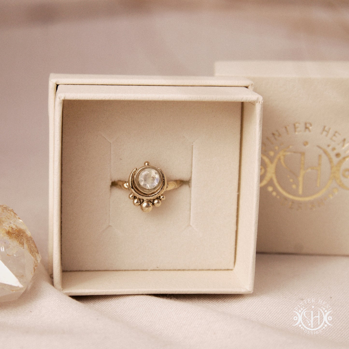 Handmade crescent moon ring with round moonstone set inside the lunar curve, in branded jewelry box.