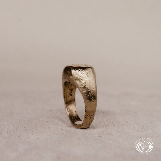 Sigil Ring handmade sandcast brass signet-style ring with raw surface and ancient-inspired sculptural form, in sand.