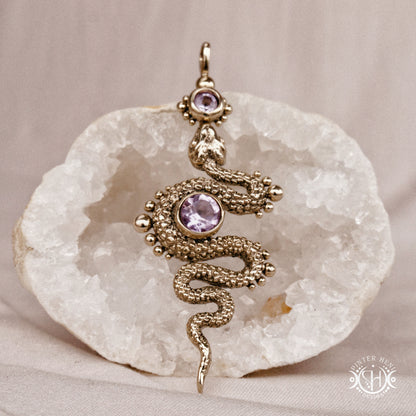 Decorative snake-shaped pendant with amethyst on a stone surface
