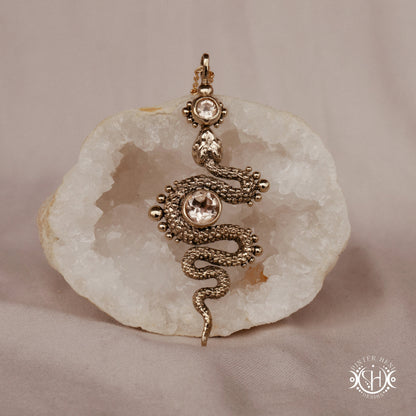 Decorative snake-shaped pendant with morganite on a stone surface