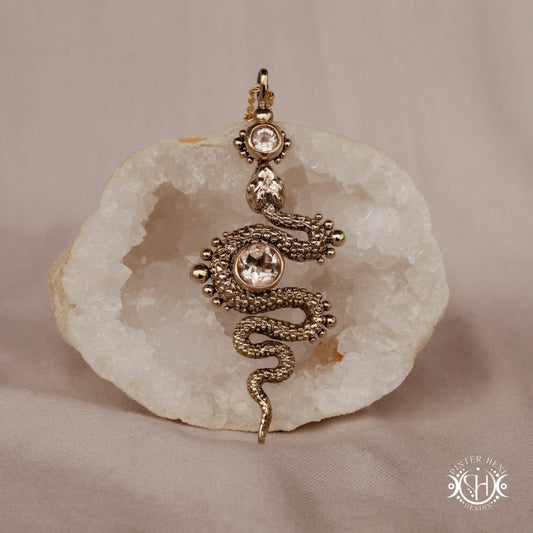 Decorative snake-shaped pendant with morganite on a stone surface
