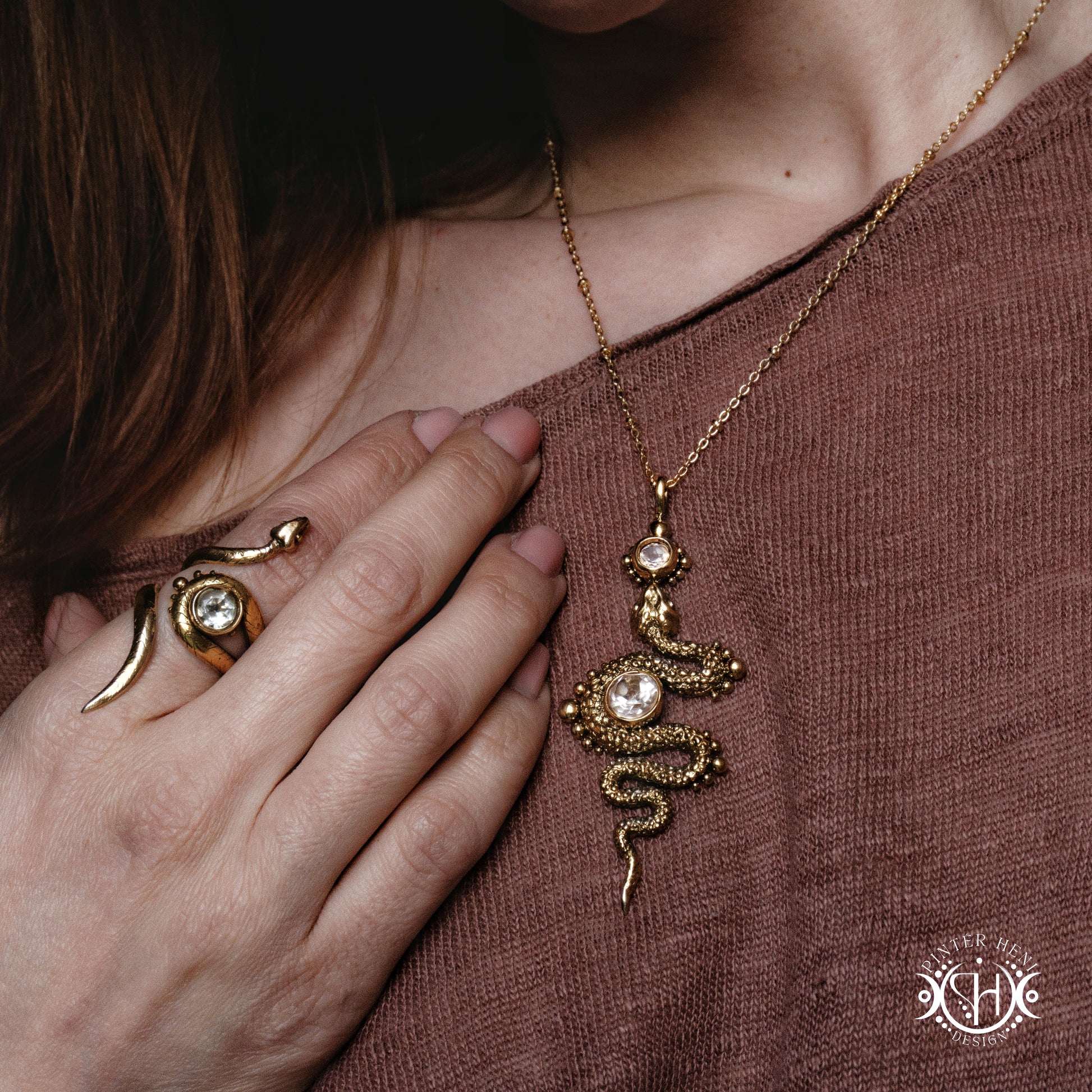 Gold snake necklace and ring on a person wearing a brown top.