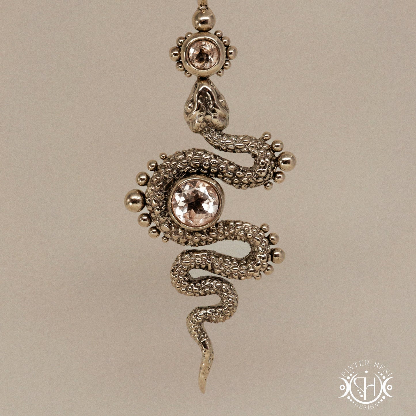 Textured snake-shaped pendant with morganite on a beige background
