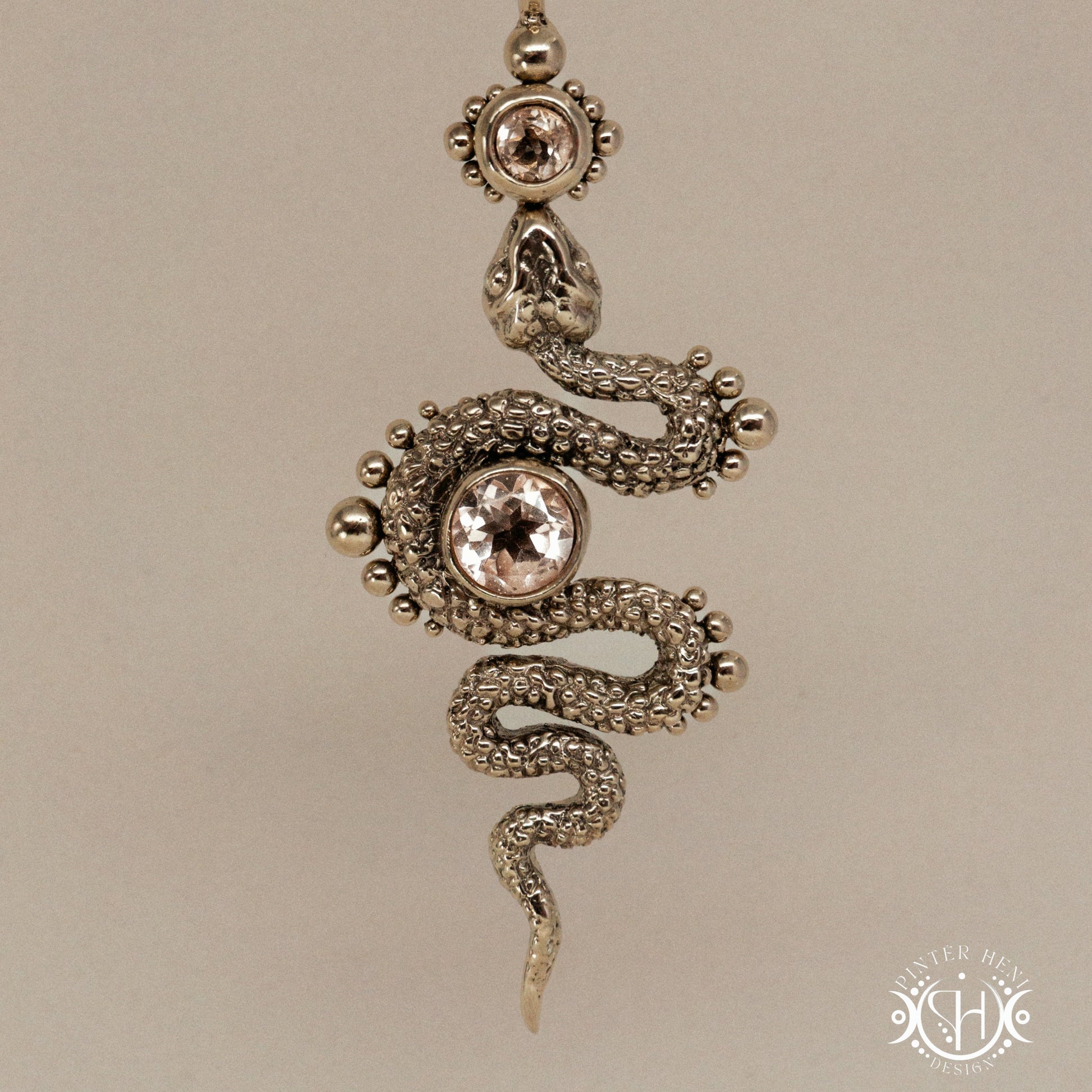 Textured snake-shaped pendant with morganite on a beige background
