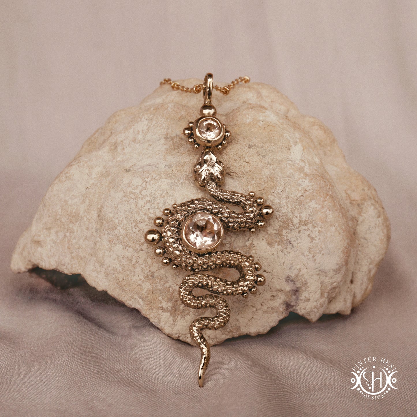 Brass snake-shaped pendant with morganite on a textured stone surface