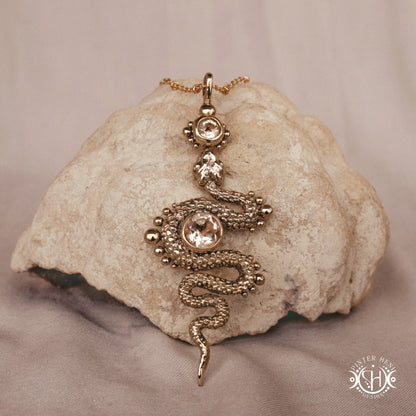 Brass snake-shaped pendant with morganite on a textured stone surface