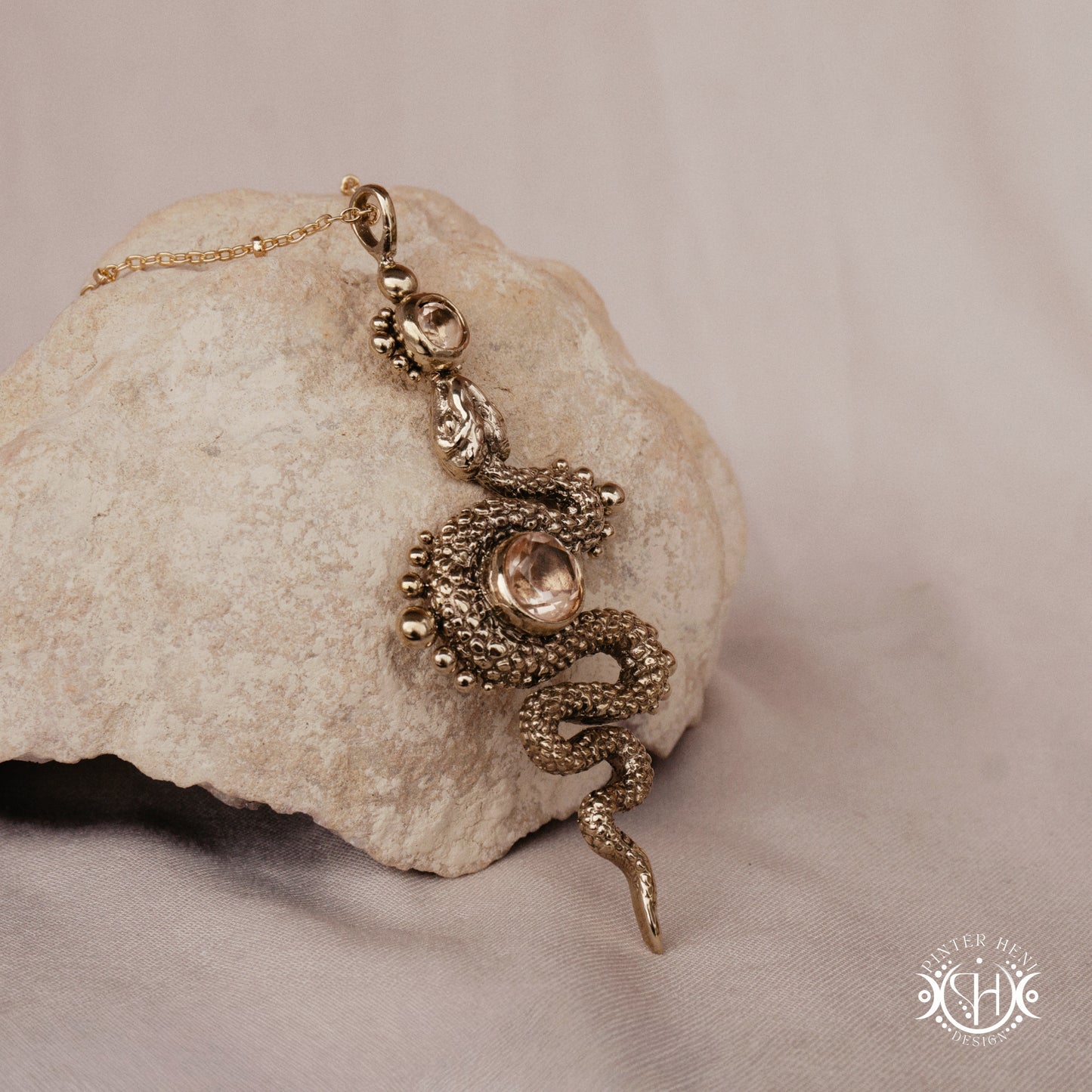 Brass snake-shaped pendant on a stone surface with a beige background