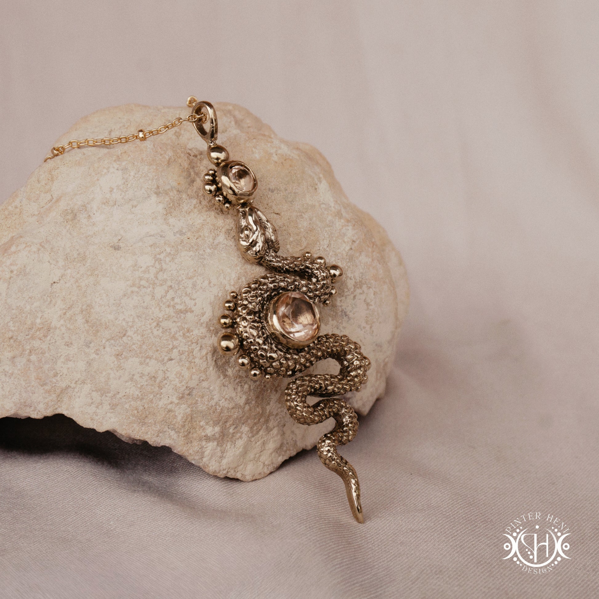 Brass snake-shaped pendant on a stone surface with a beige background
