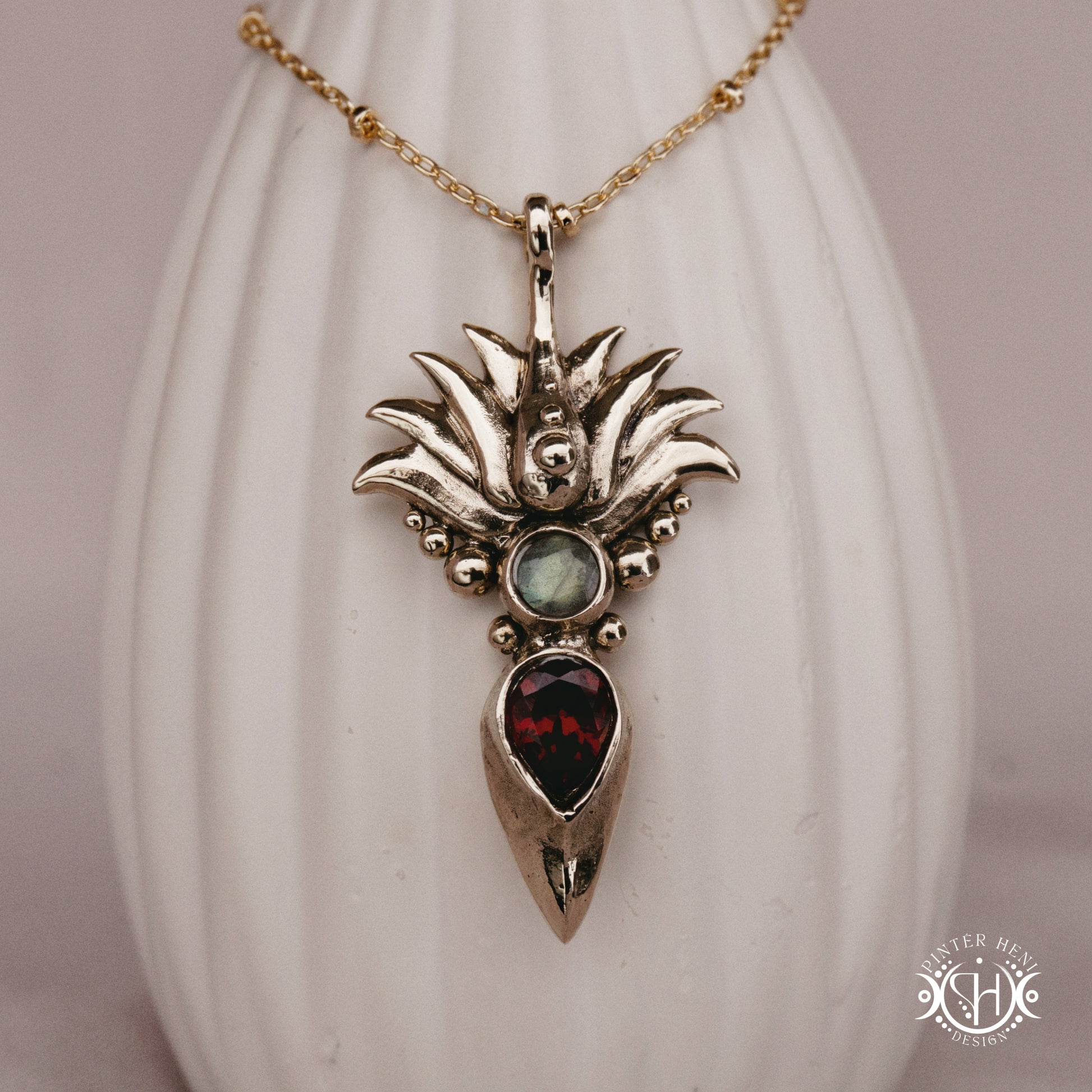 Handmade Agave pendant with garnet stone, sculptural desert-inspired botanical necklace, on ceramic vase.