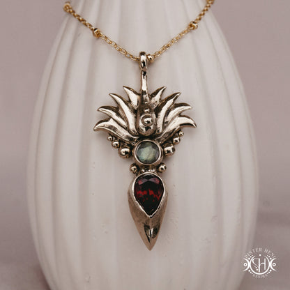 Handmade Agave pendant with garnet stone, sculptural desert-inspired botanical necklace, on ceramic vase.