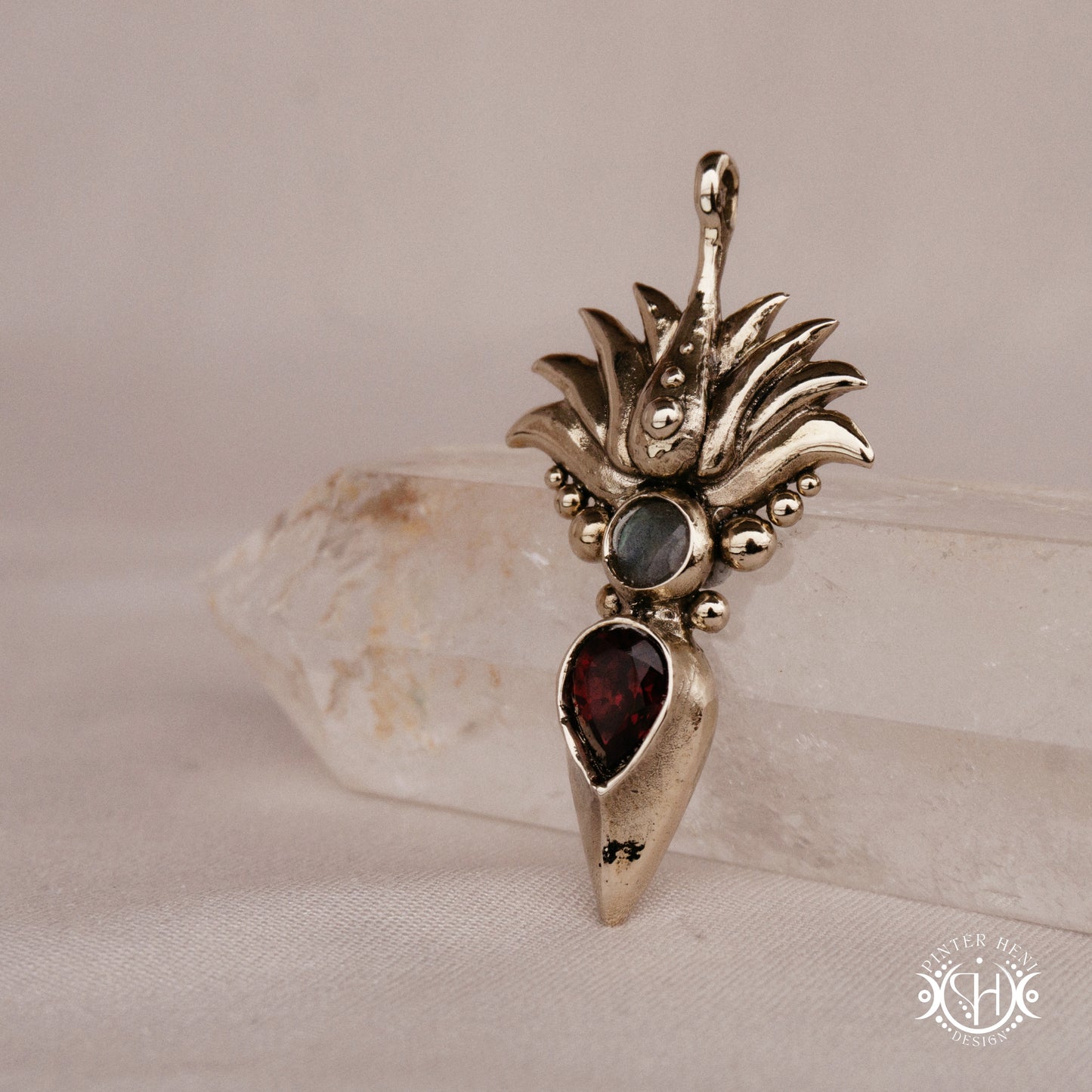 Handmade Agave pendant with garnet stone, sculptural desert-inspired botanical necklace, on crystal, side view.