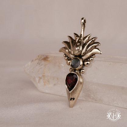 Handmade Agave pendant with garnet stone, sculptural desert-inspired botanical necklace, on crystal, side view.
