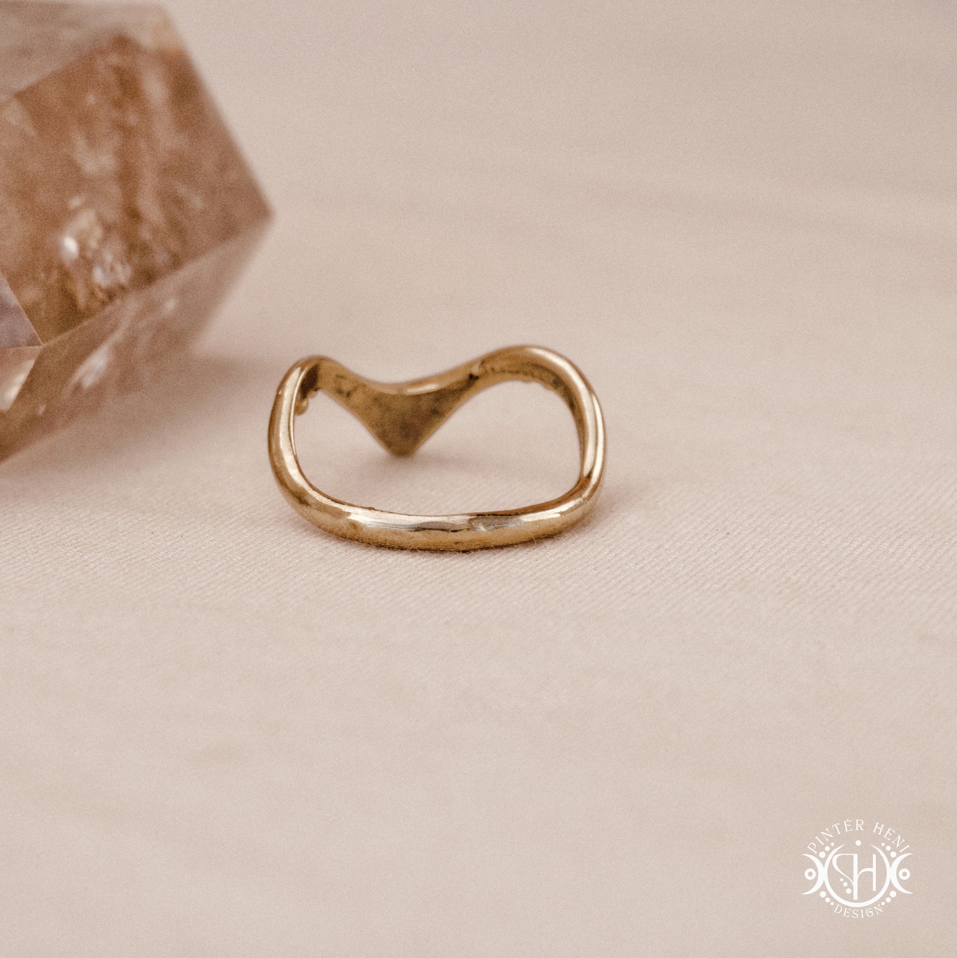 Arc Ring organic sculptural wave ring handmade in brass with rounded nodular details, on beige surface.