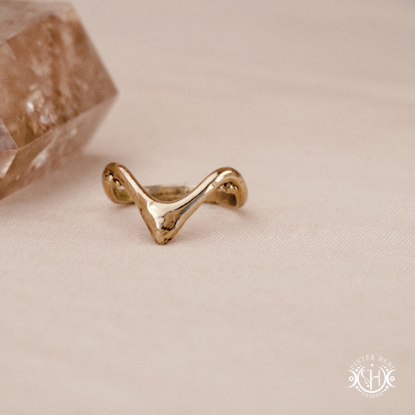 Arc Ring organic sculptural wave ring handmade in brass with rounded nodular details, on beige surface.