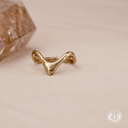 Arc Ring organic sculptural wave ring handmade in brass with rounded nodular details, on beige surface.