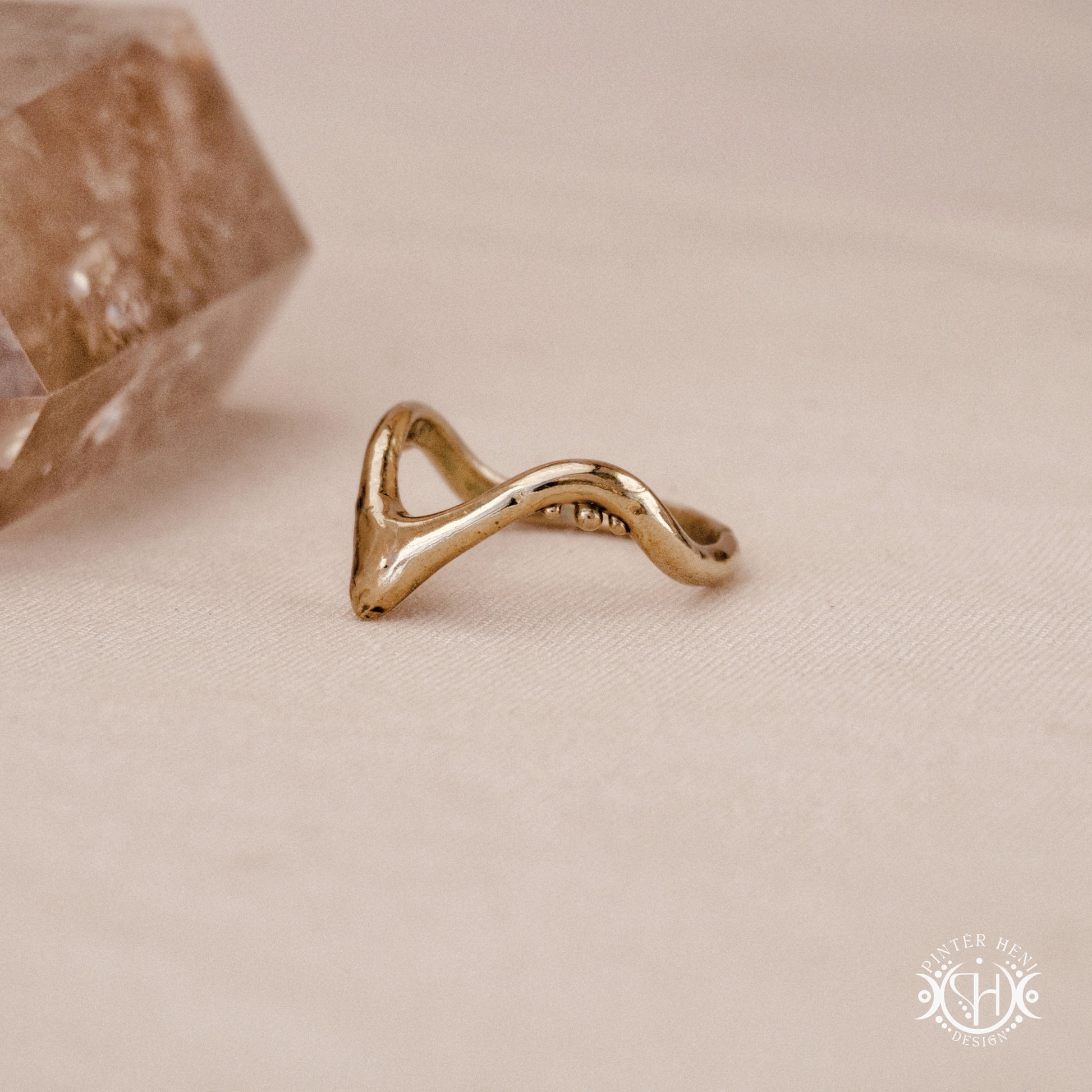 Arc Ring organic sculptural wave ring handmade in brass with rounded nodular details, on beige surface.