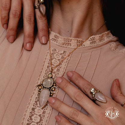 Close-up of a person wearing a necklace with a pendant and multiple rings on a lace-trimmed garment.