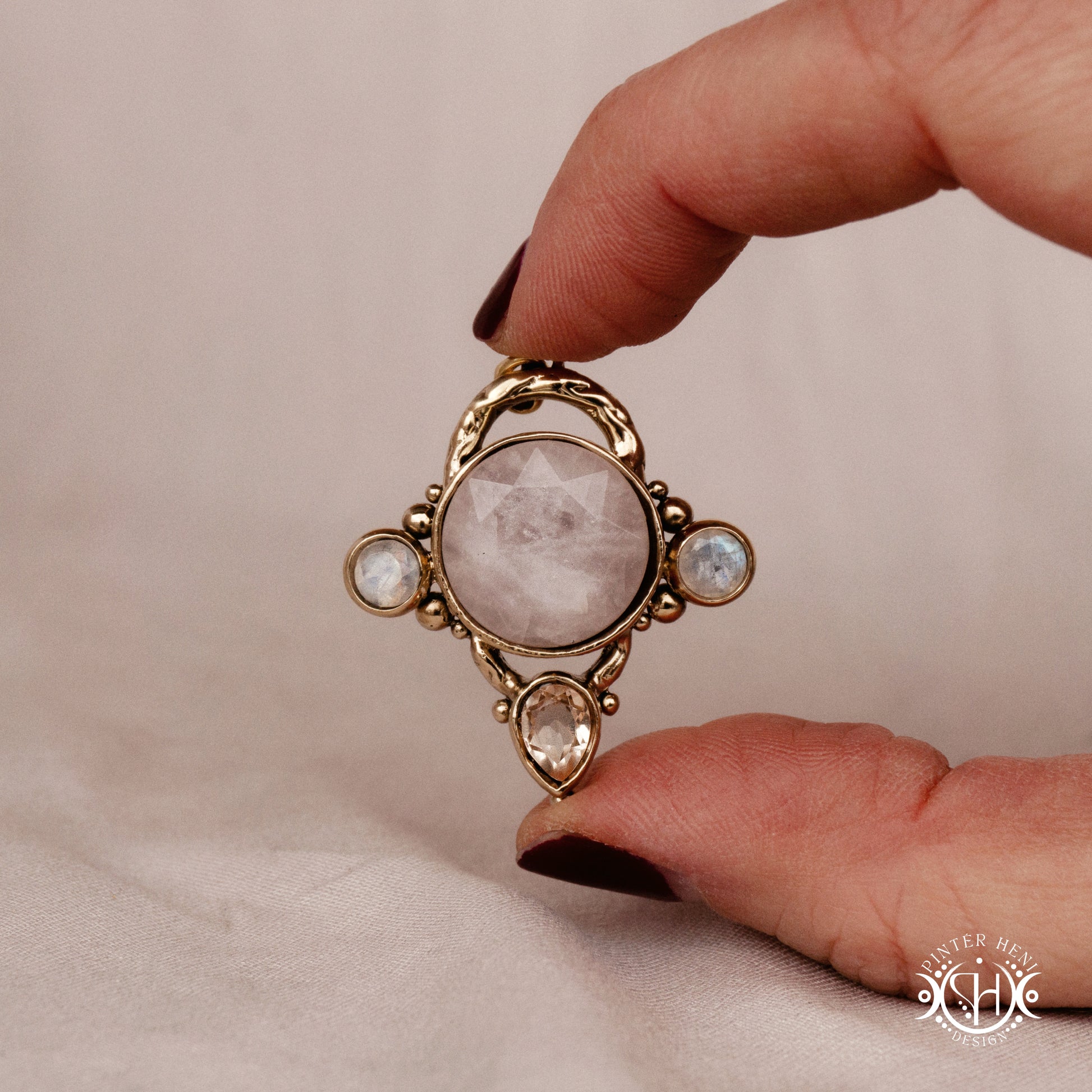 Handmade brass pendant with moonstone, morganite and rose quartz, held in hand