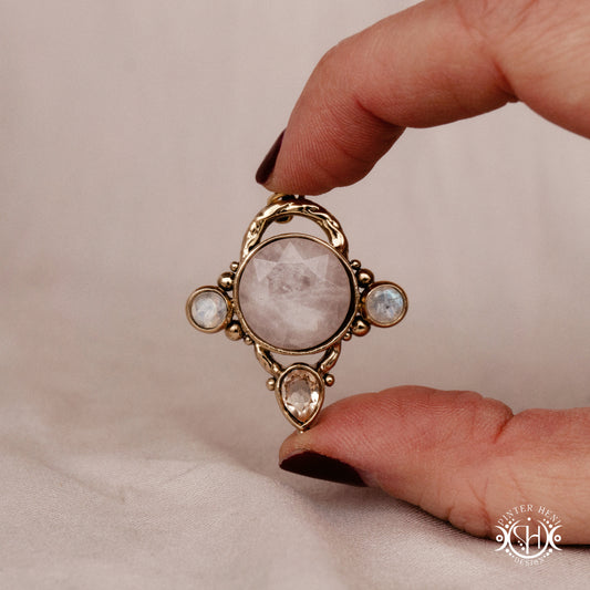 Handmade brass pendant with moonstone, morganite and rose quartz, held in hand