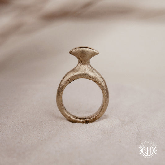 Glyph Ring handmade sandcast brass ring with curved sculptural top and ancient symbolic character, on sand.