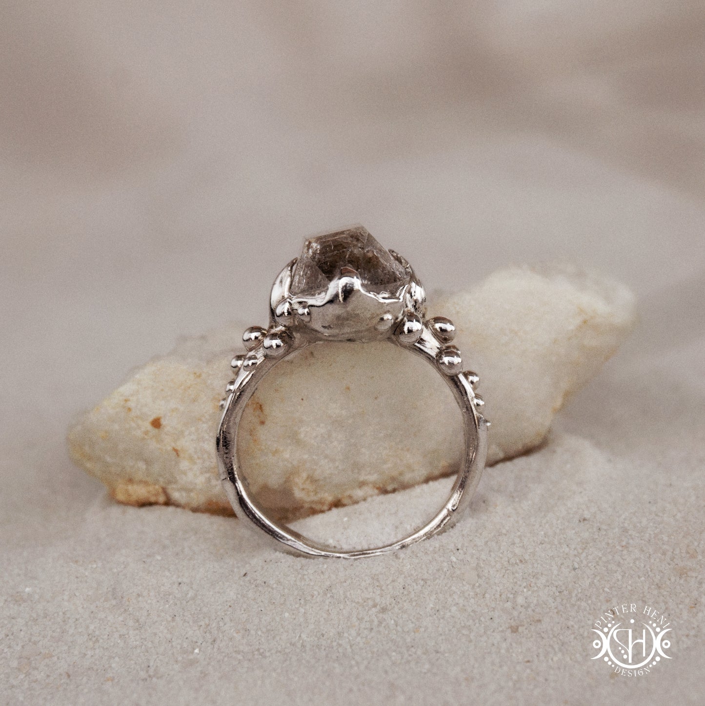 Silver ring with a large stone on a rock in sand
