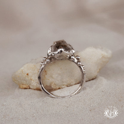 Silver ring with a large stone on a rock in sand