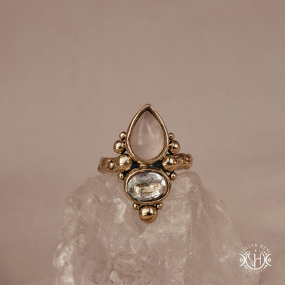 Handmade Kore ring with rose quartz and aquamarine in balanced sculptural setting, on crystal