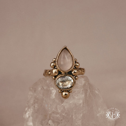 Handmade Kore ring with rose quartz and aquamarine in balanced sculptural setting, on crystal