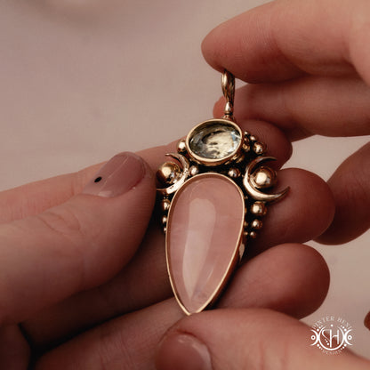 Hand-carved Nyx pendant with rose quartz and prasiolite, held in hand.
