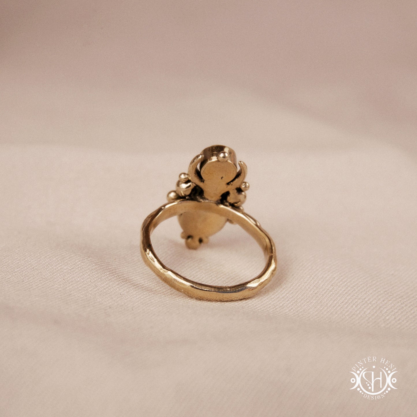 Hand-carved Nyx ring with opal and moonstone in brass, sculptural crescent design, on beige surface.
