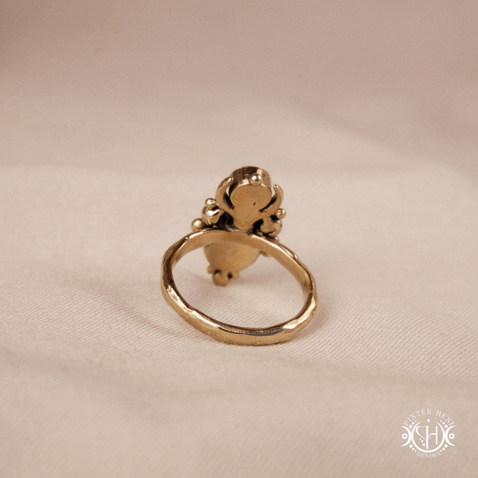 Hand-carved Nyx ring with opal and moonstone in brass, sculptural crescent design, on beige surface.
