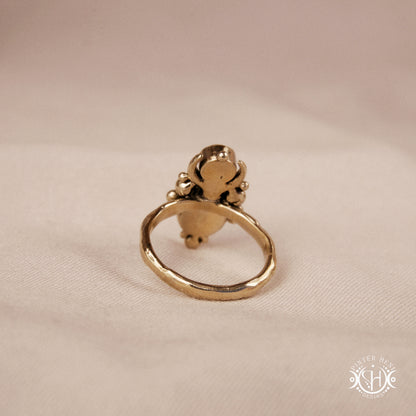Hand-carved Nyx ring with opal and moonstone in brass, sculptural crescent design, on beige surface.
