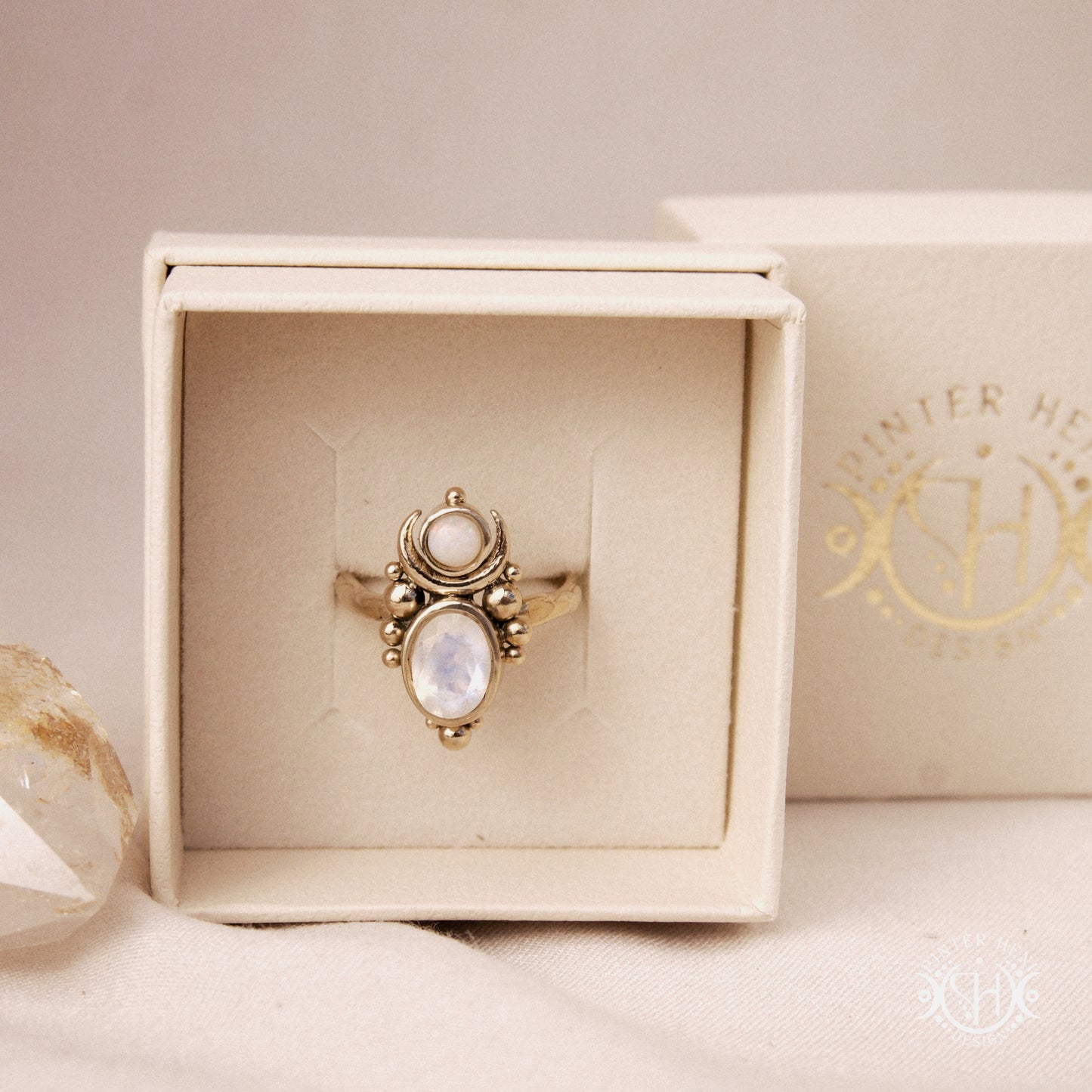 Hand-carved Nyx ring with opal and moonstone in brass, sculptural crescent design, in jewelry box.