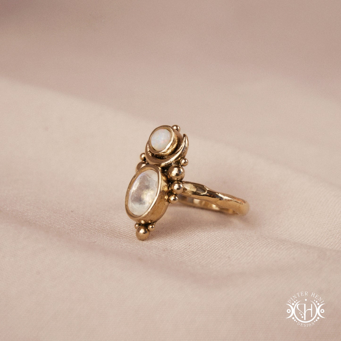 Hand-carved Nyx ring with opal and moonstone in brass, sculptural crescent design, on beige surface.

