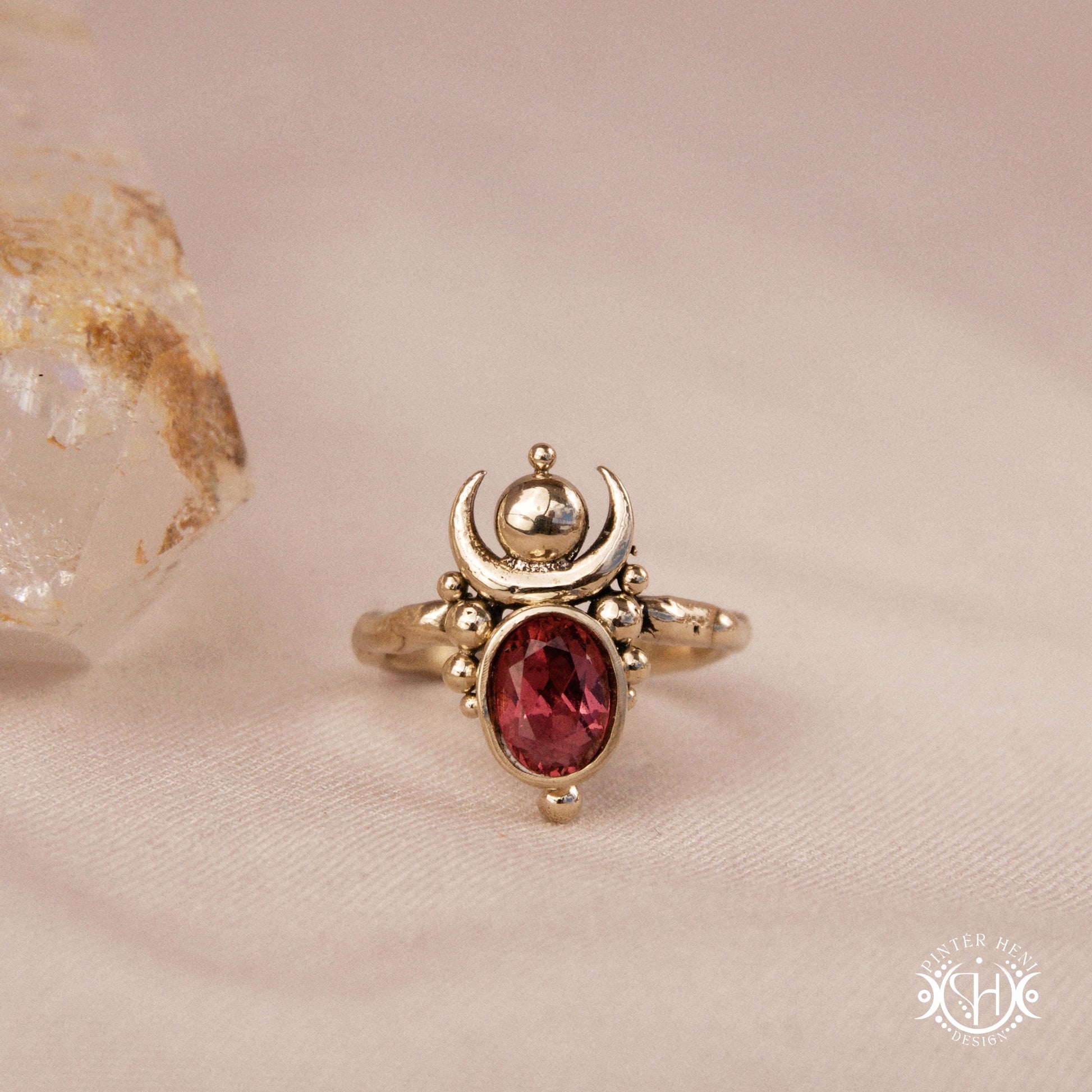 Hand-carved Nyx ring with opal and garnet, compact vertical sculptural form, on beige surface.