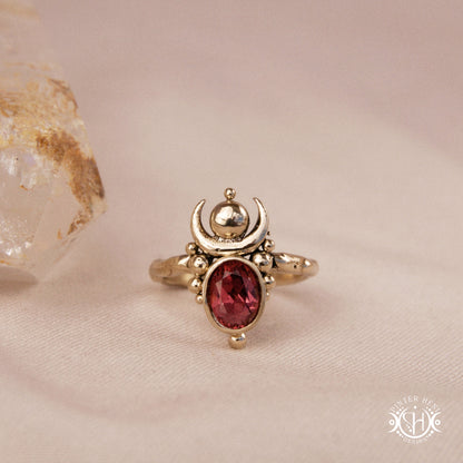Hand-carved Nyx ring with opal and garnet, compact vertical sculptural form, on beige surface.
