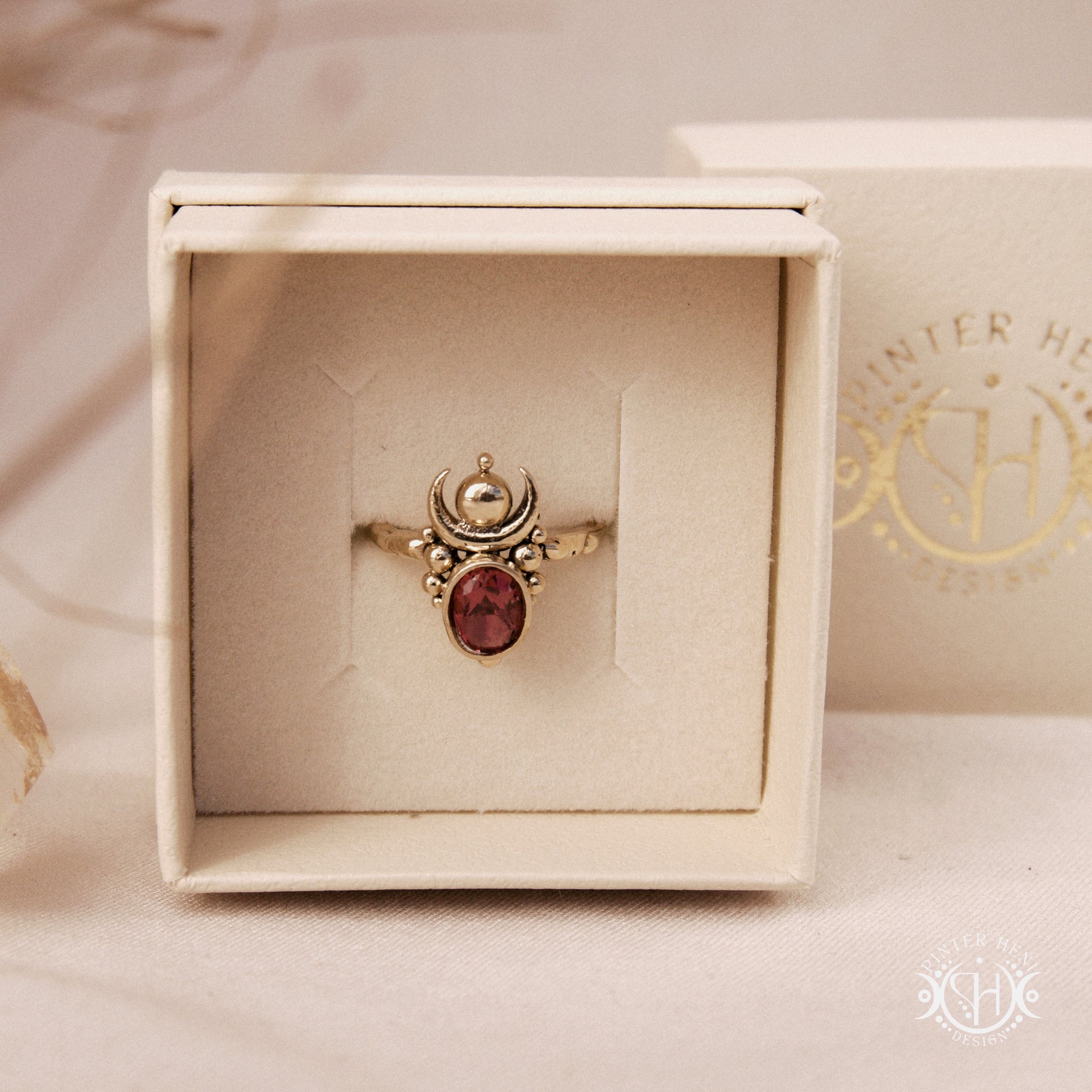 Hand-carved Nyx ring with opal and garnet, compact vertical sculptural form, in jewelry box.