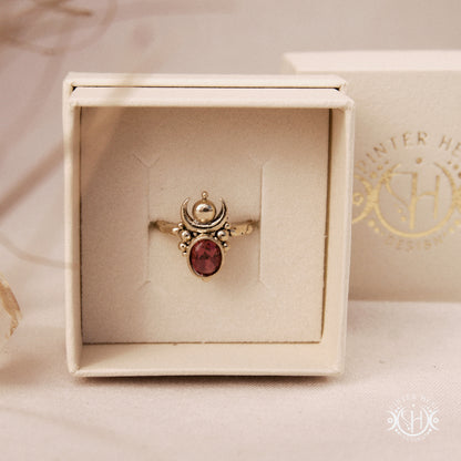 Hand-carved Nyx ring with opal and garnet, compact vertical sculptural form, in jewelry box.