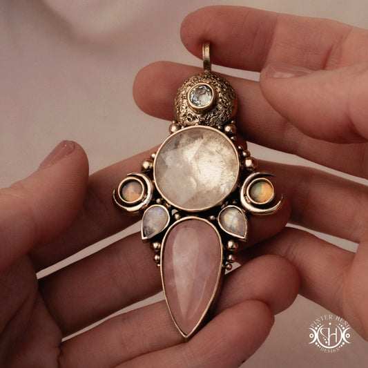 Hand-carved Persephone pendant with opal, moonstone, prasiolite and rose quartz, held in hand.