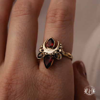 Handmade Persephone ring with garnet and green tourmaline in sculptural feminine setting, worn on hand.