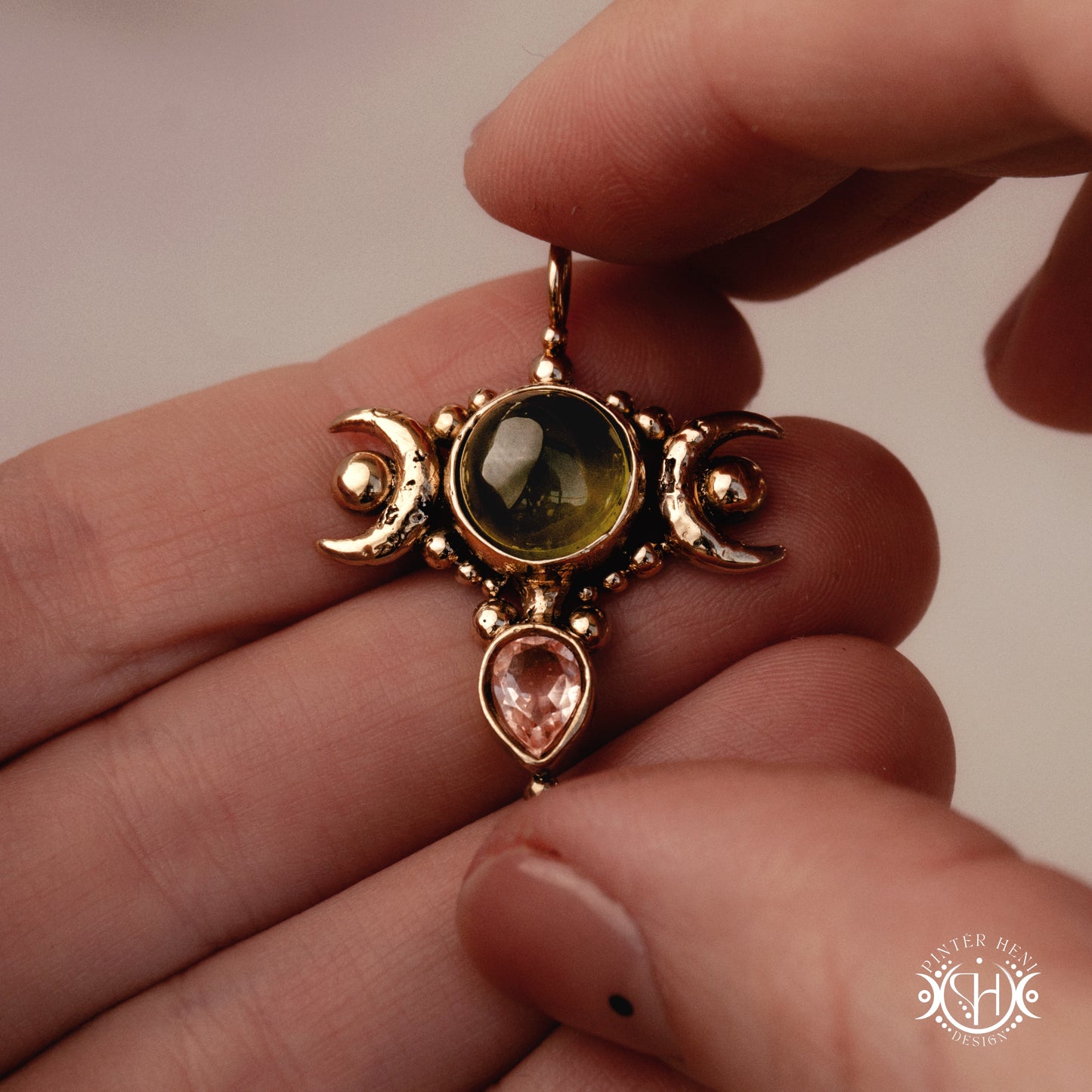 Hand-carved Selene crescent pendant with vesuvianite and morganite, held in hand.