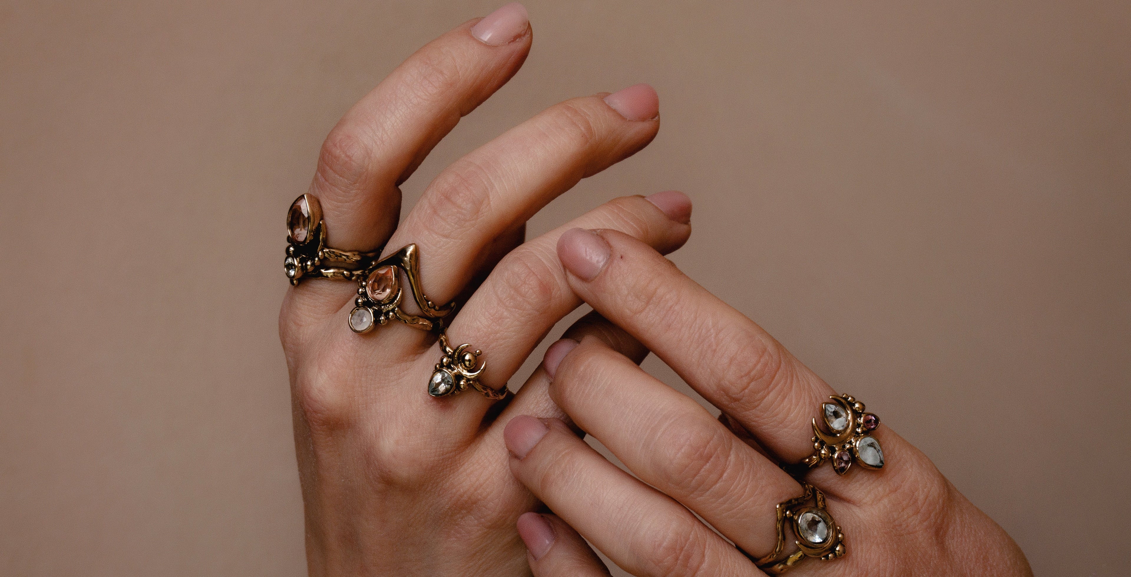 Handcrafted rings with precious stones worn on hands, on beige backround