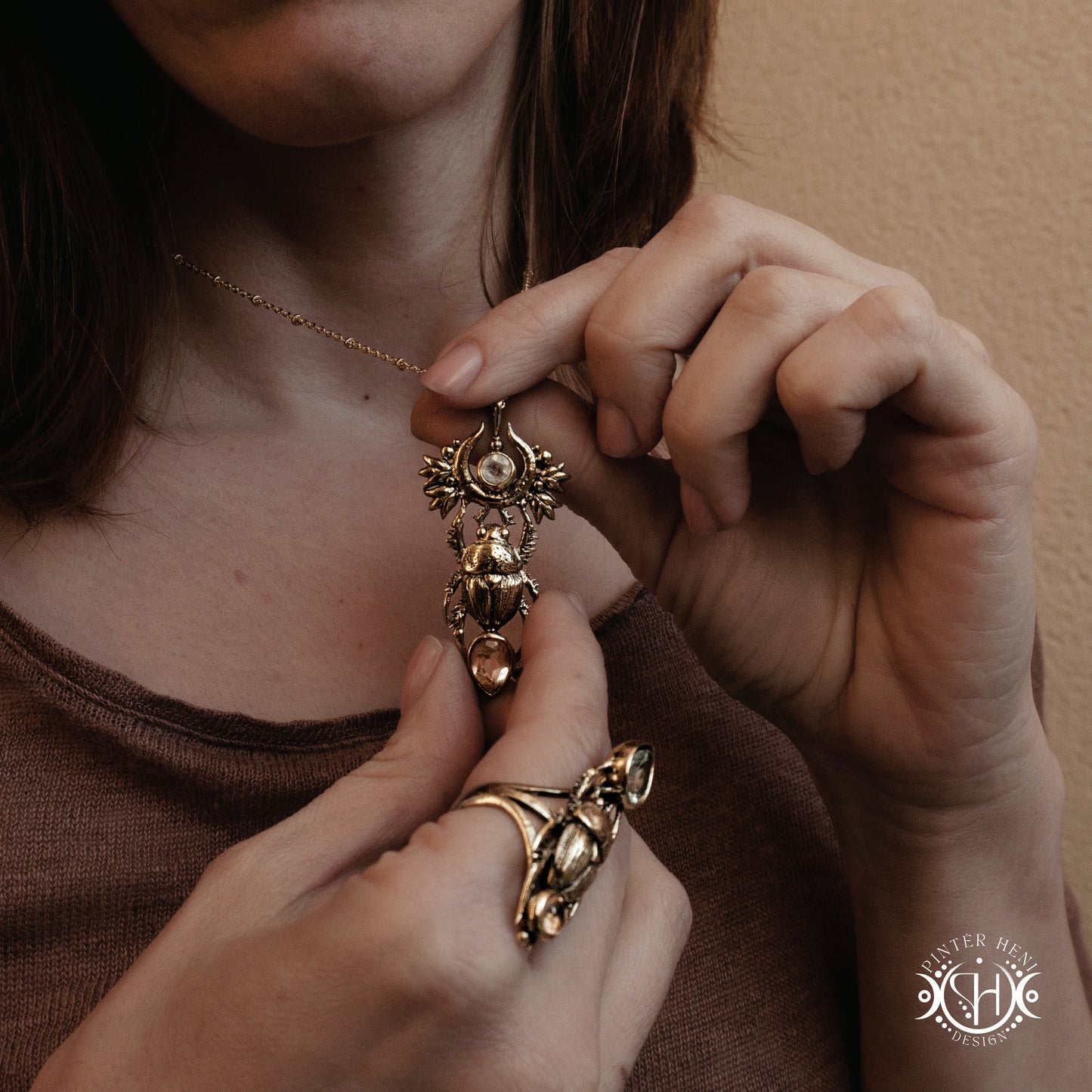 
Close-up of a person wearing a gold scarab necklace and ring, with a blurred background.