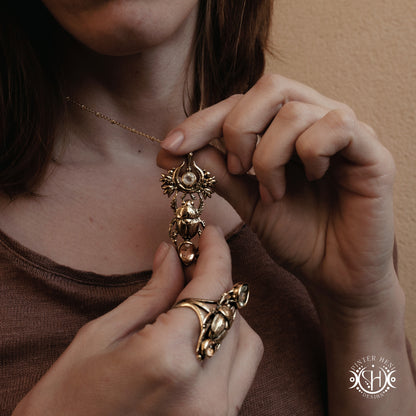 
Close-up of a person wearing a gold scarab necklace and ring, with a blurred background.
