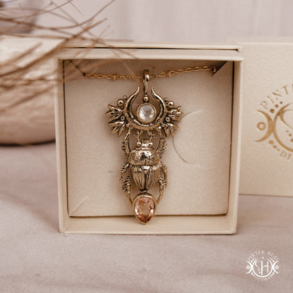 Brass scarab pendant with gemstones in a decorative box on a beige surface