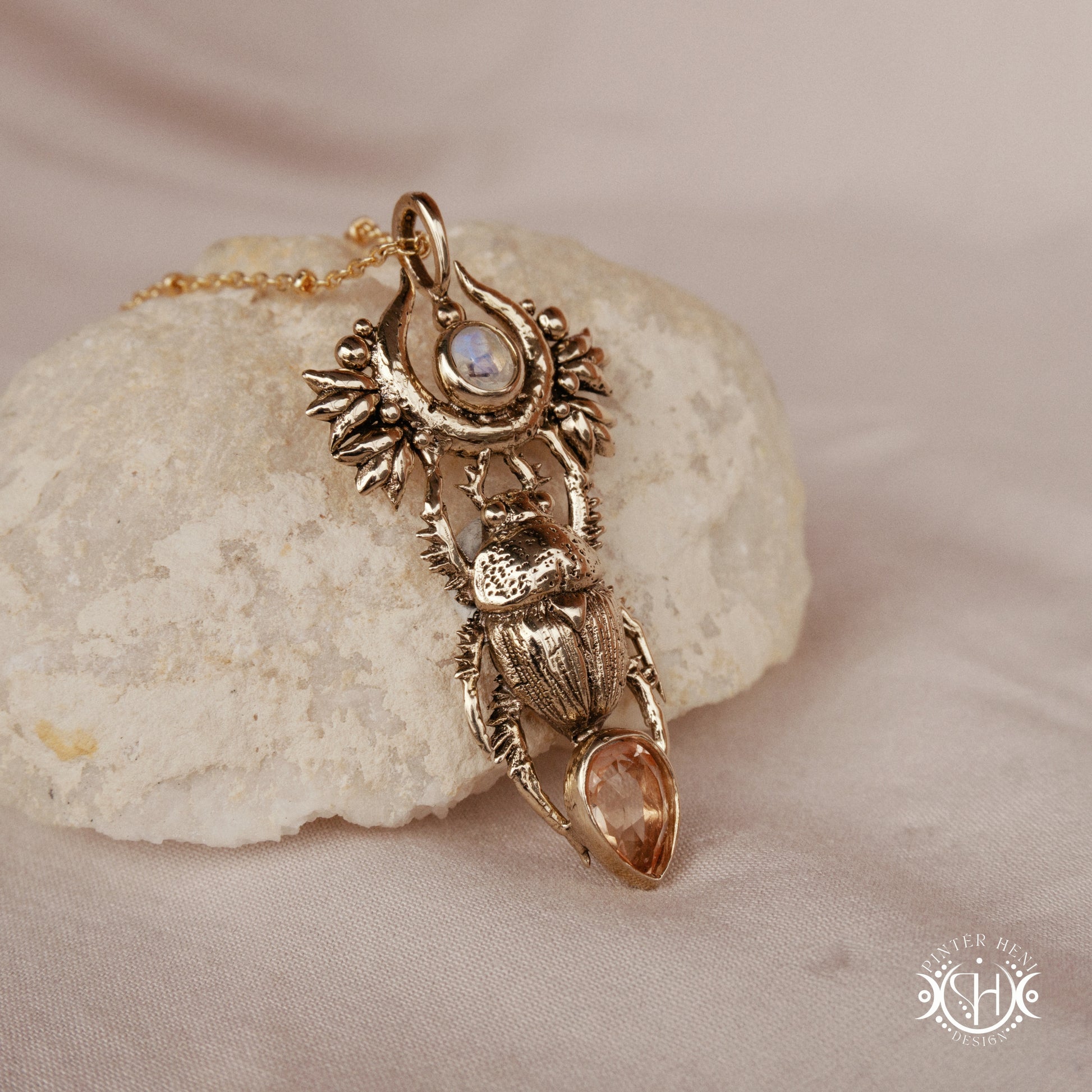 Scarab pendant in brass with moonstone and morganite, side view, on a textured stone surface