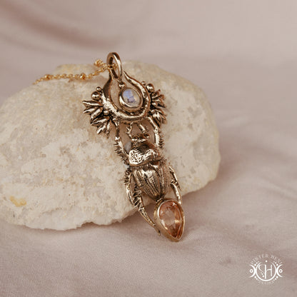 Scarab pendant in brass with moonstone and morganite, side view, on a textured stone surface