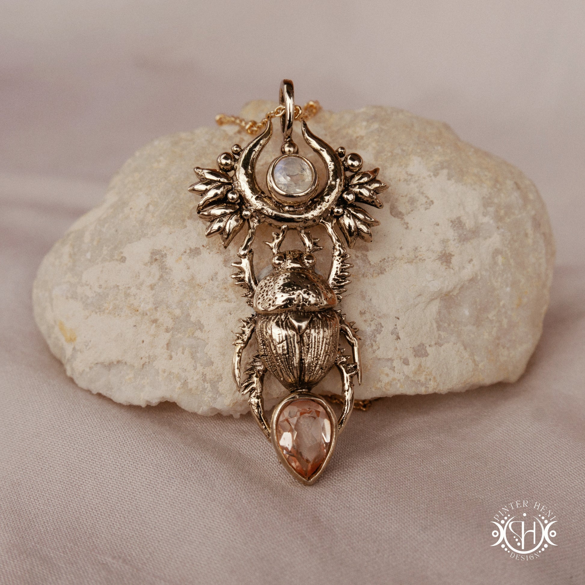 Scarab pendant in brass with moonstone and morganite, front view, on a stone surface 