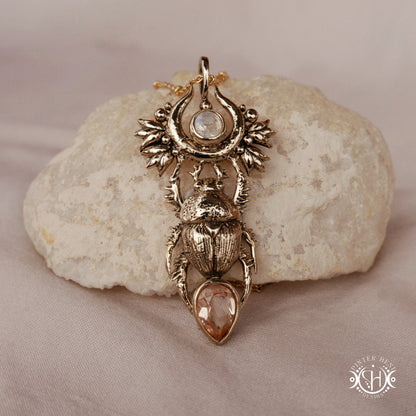Scarab pendant in brass with moonstone and morganite, front view, on a stone surface 
